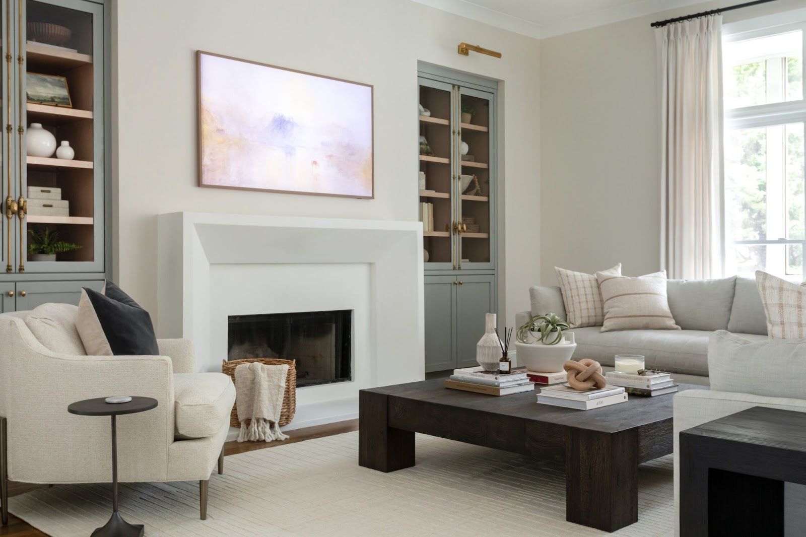 a cozy living room with blue built-in shelving and cabinets, square wood coffee table, and off-white couches and chairs. 